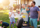 Vaderdag in het buitenland: een gezellige BBQ met generaties, waar een vader geniet van een drankje terwijl zijn kind en ouder samen plezier hebben in de tuin.