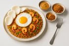 Een bord met Hollandse nasi goreng, afgewerkt met een gebakken ei, garnalen, en geserveerd met seroendeng, satésaus en gebakken uitjes. Perfect bij het recept: Simpele, Hollandse Nasi Goreng met seroendeng en satésaus.